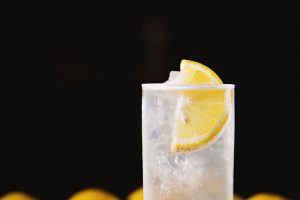 Principle close up of clear drink in a thin glass with lemon wedge in drink