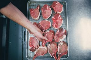 Principle shot of raw steaks on grated pan with chef placing steak on pan
