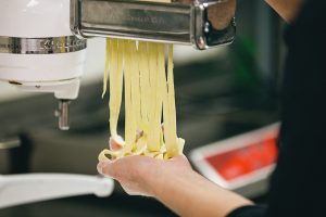 Principle medium shot of pasta noodles coming out of pasta machine with persons hand catching it