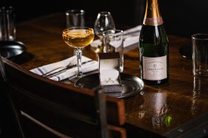 Principle shot of restaurant table with wine glasses and bottle of wine with a plate in front of it wedding ring inside ring box on top of plate